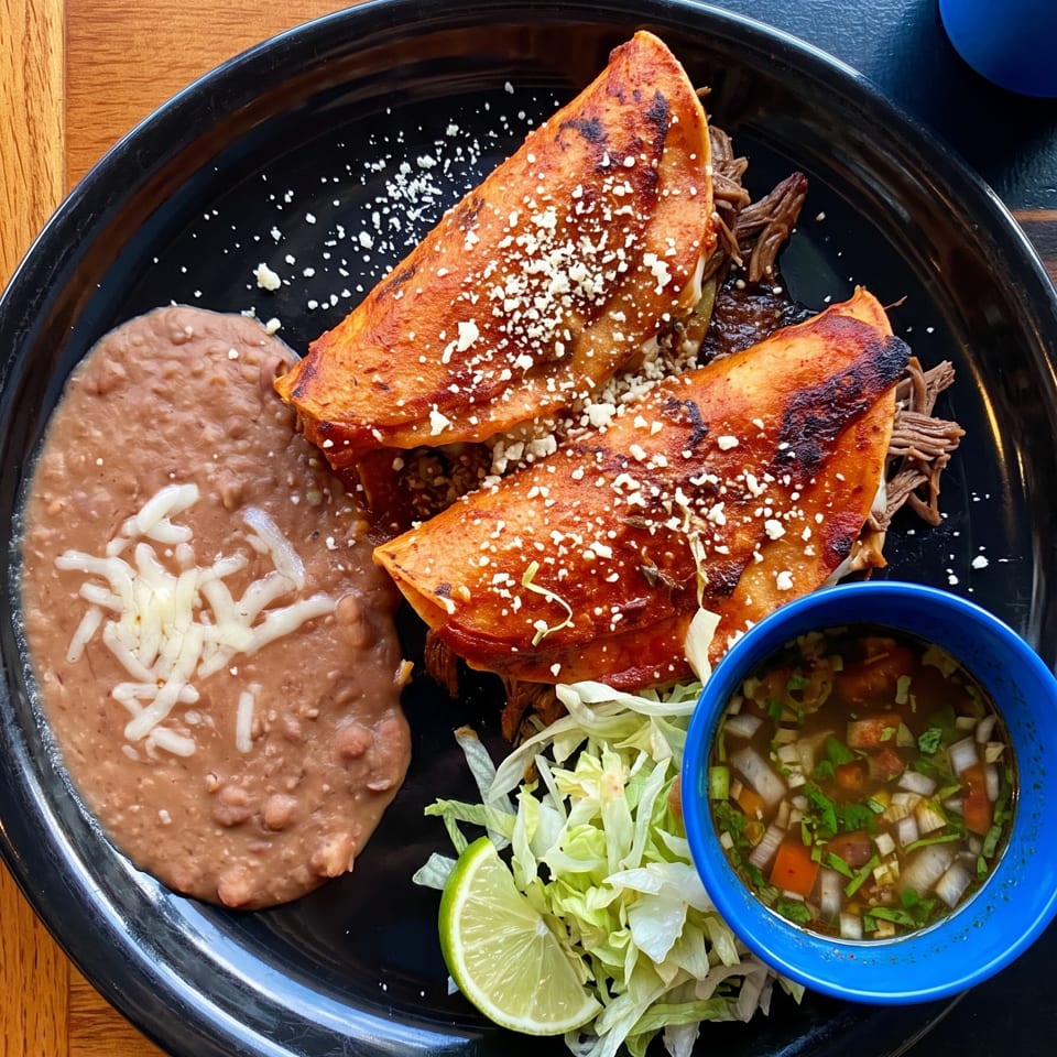 Mexican platter with two cheese-topped shredded beef enchiladas, refried beans, lettuce, lime, and salsa.
