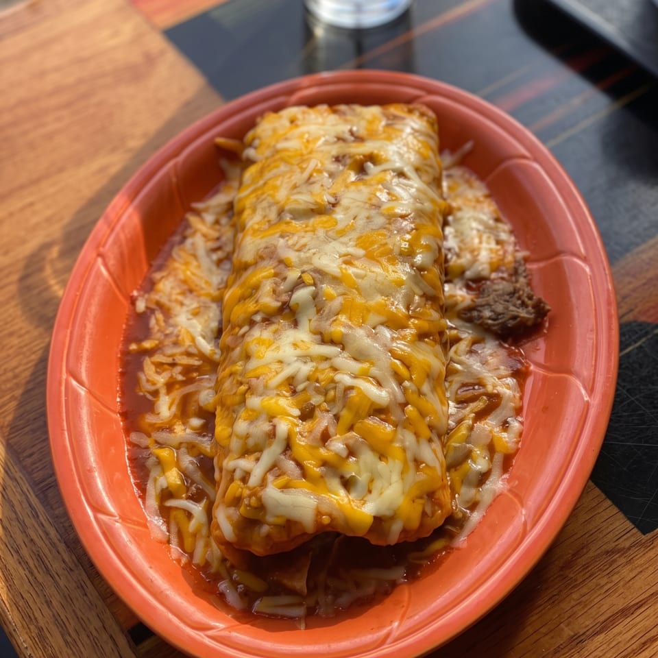 Cheesy enchiladas smothered in melted cheese and sauce, served with rice and beans on a red plate.