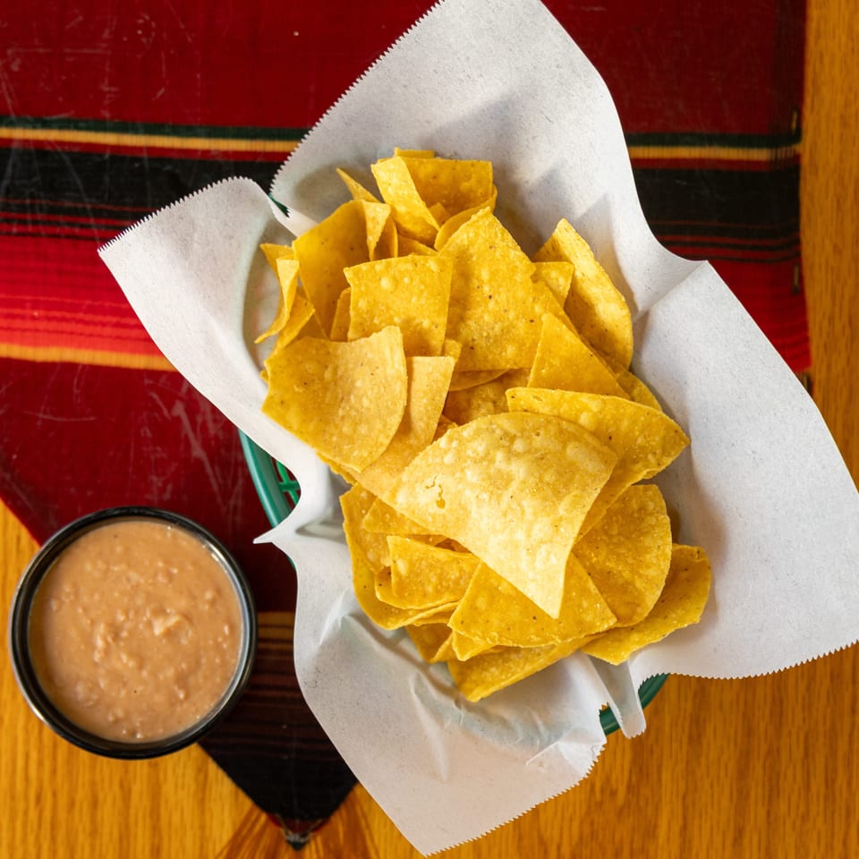 Basket of golden tortilla chips with a side of refried beans on a colorful restaurant table.