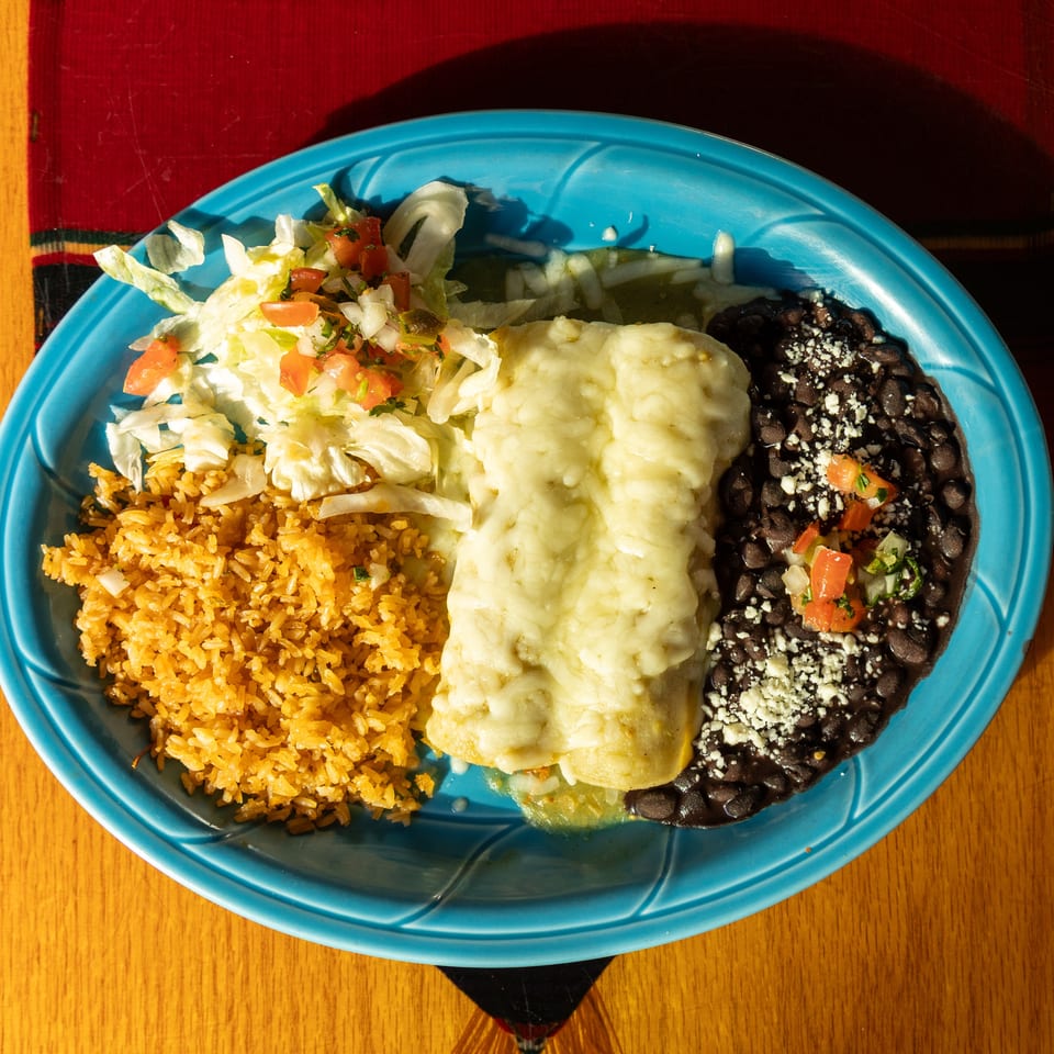 Mexican combination plate with cheesy enchiladas, Spanish rice, black beans, and lettuce salad topped with pico de gallo.