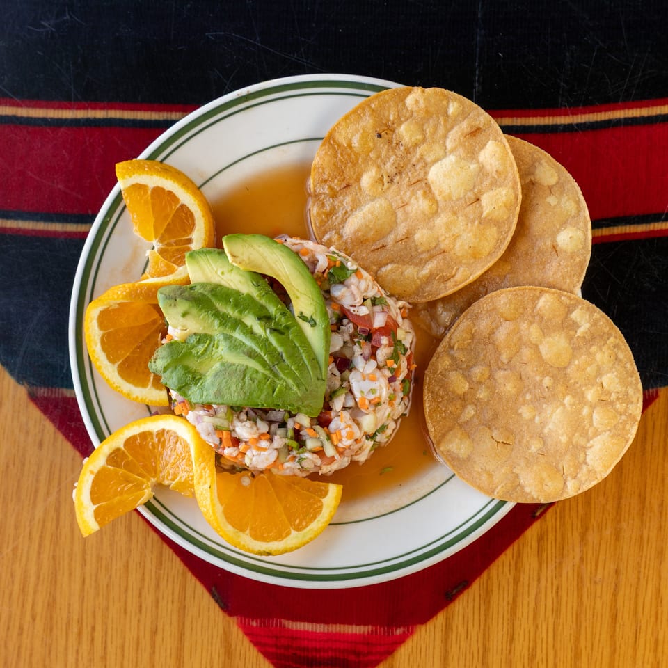 Plate of shrimp ceviche topped with avocado, surrounded by orange slices and crispy tostadas.